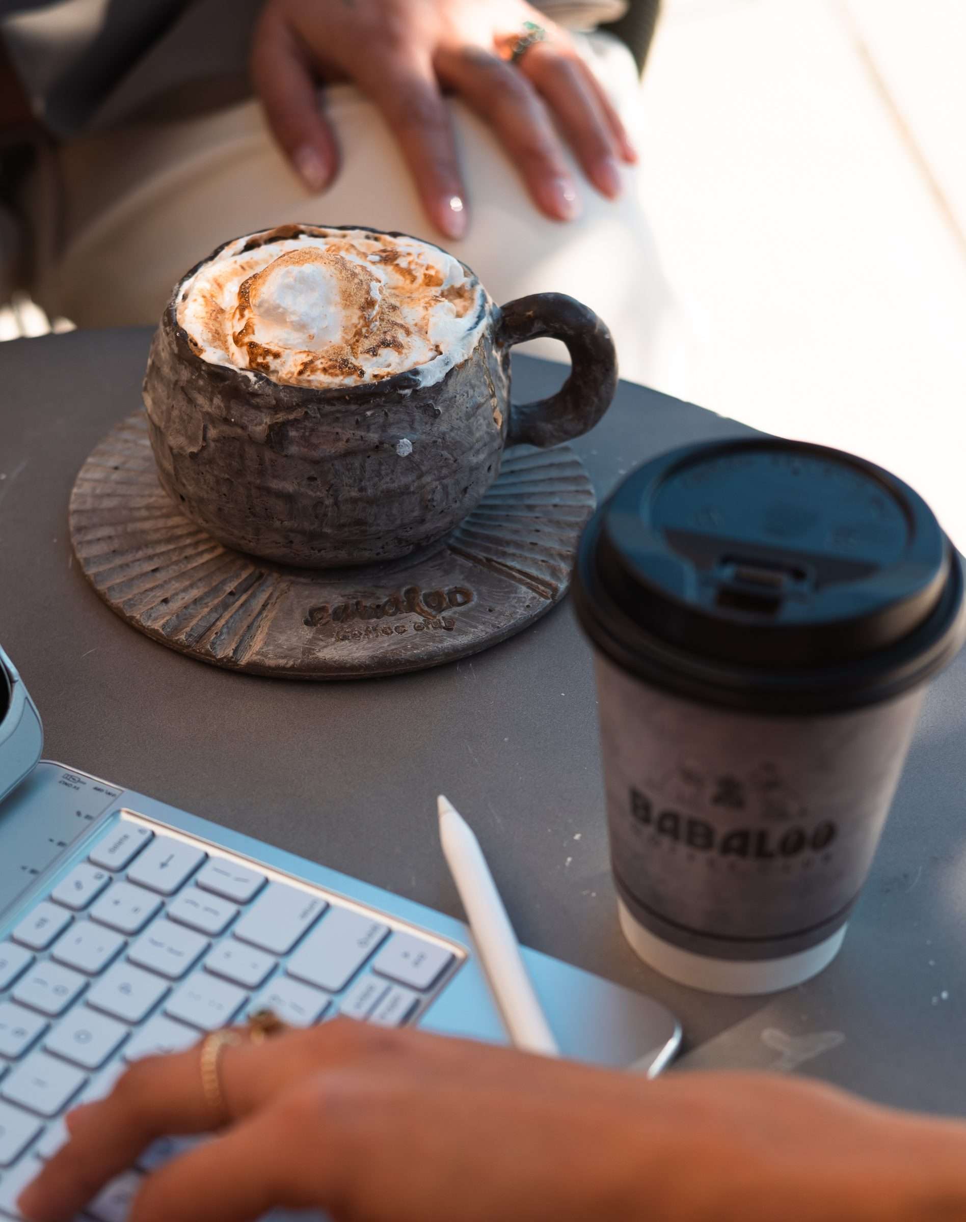 Latte in a stoneware cup and a Babaloo to-go cup on a café table